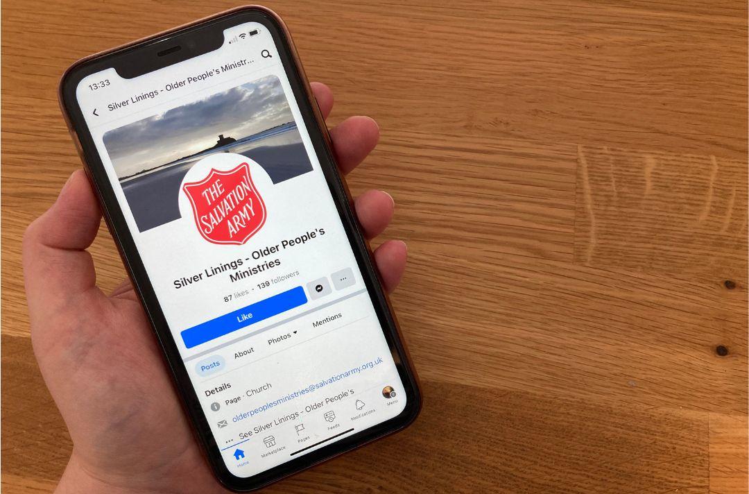Someone holding a phone and looking at a Facebook group called 'Silver Linings - Older People's Ministries' with a photo of The Salvation Army's red shield