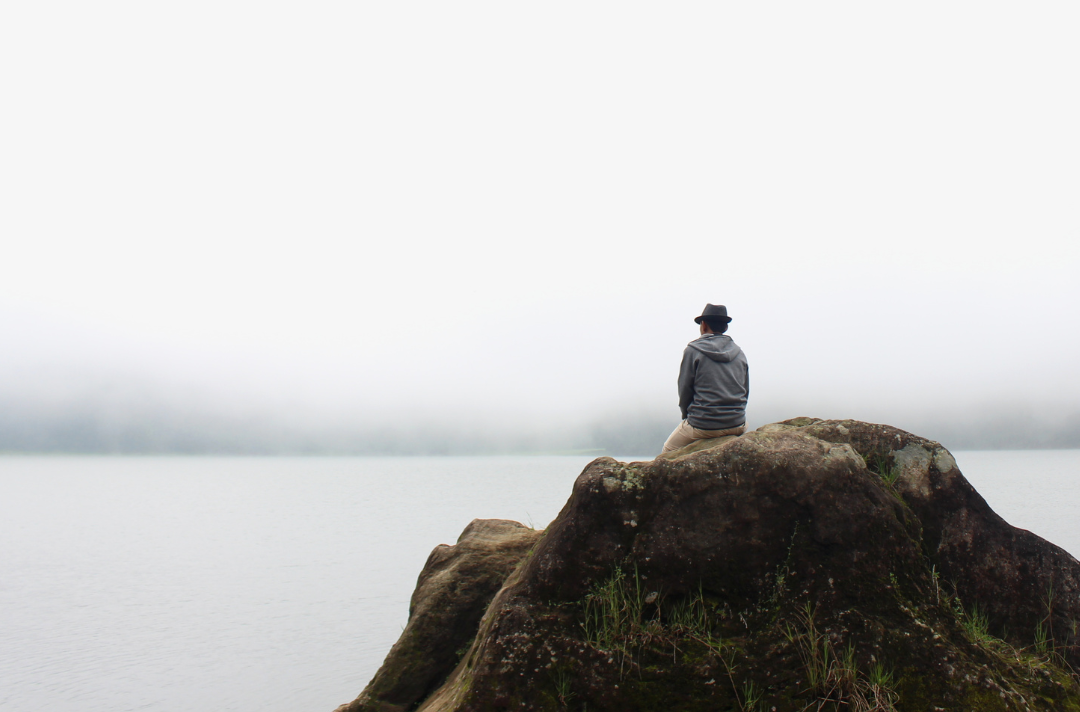 Someone sitting on a rock looking at a view of a lake