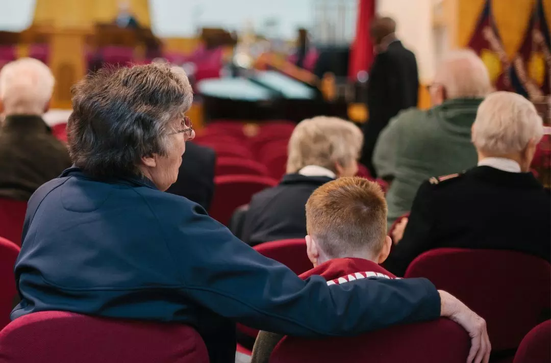 A grandparent with their army around their grandchild in a worship meeting