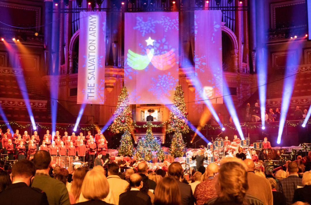 A photo of carol singing at Celebrating Christmas with The Salvation Army at the Royal Albert Hall featuring spotlights and Christmas trees.