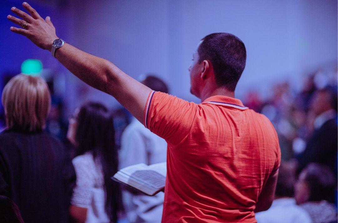A photo of someone in church praising God with their arm in the air and holding a Bible