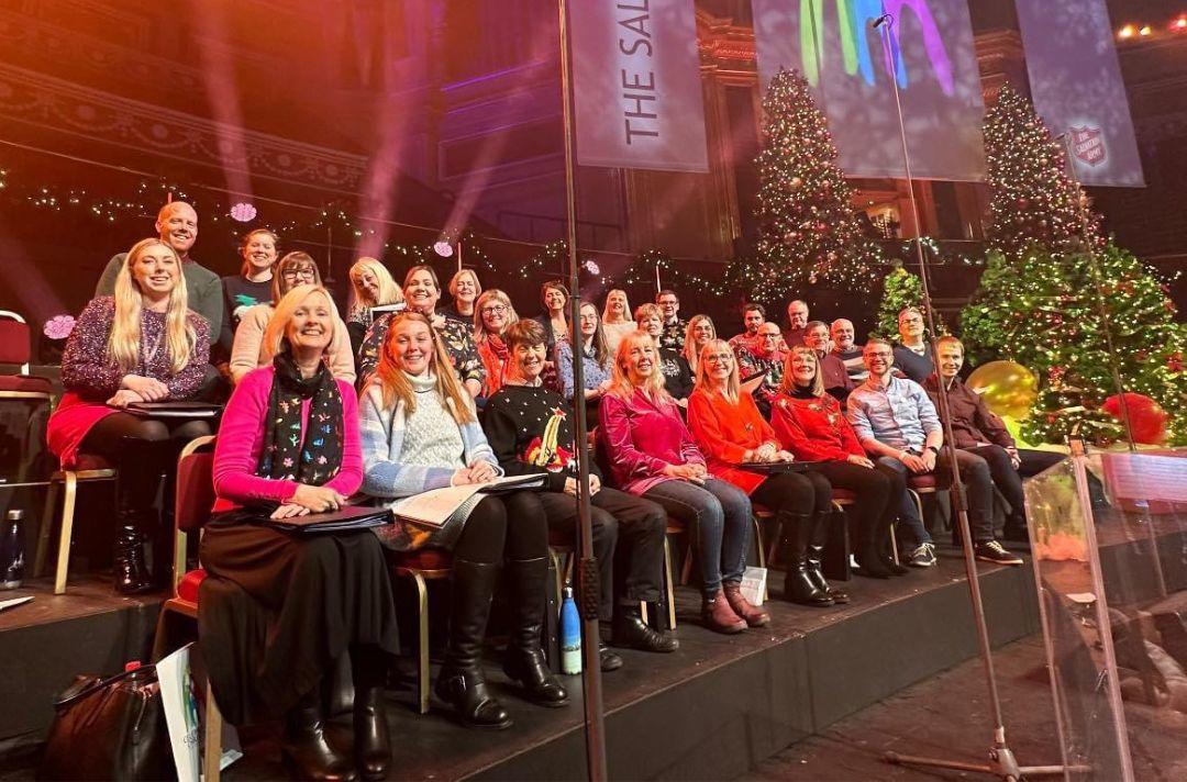 A photo of the International Staff Songsters sitting on stage and wearing Christmas jumpers
