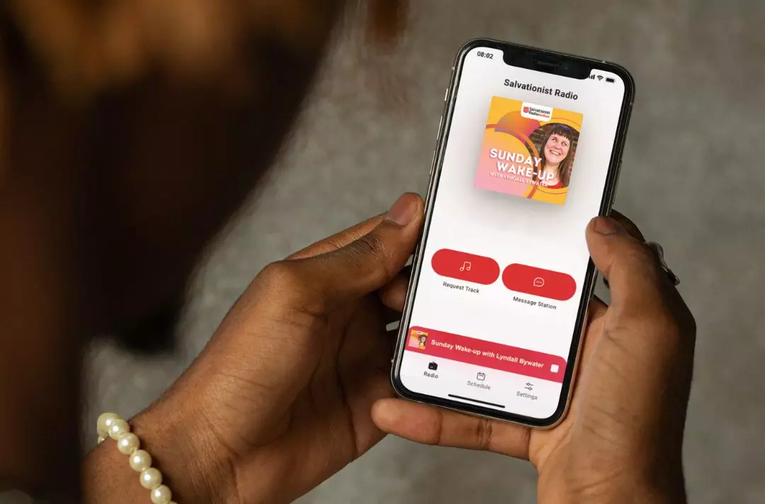 A photo of holding their phone. Their phone is displaying a Salvationist Radio podcast.
