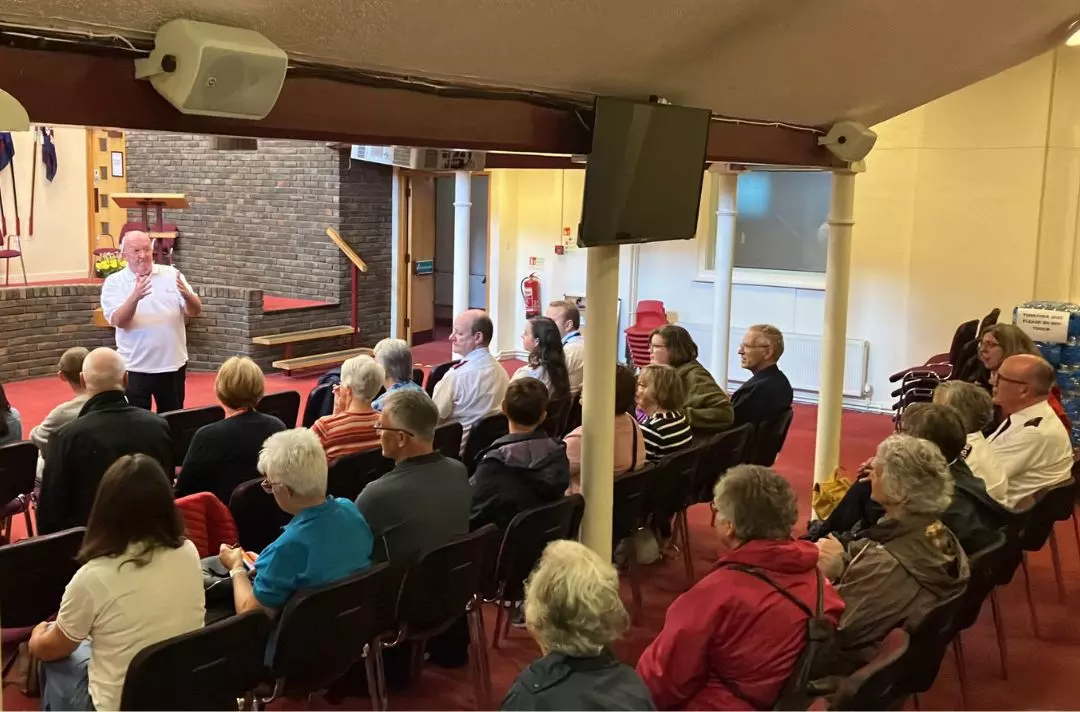 A man speaks to a group sitting in a Salvation Army hall
