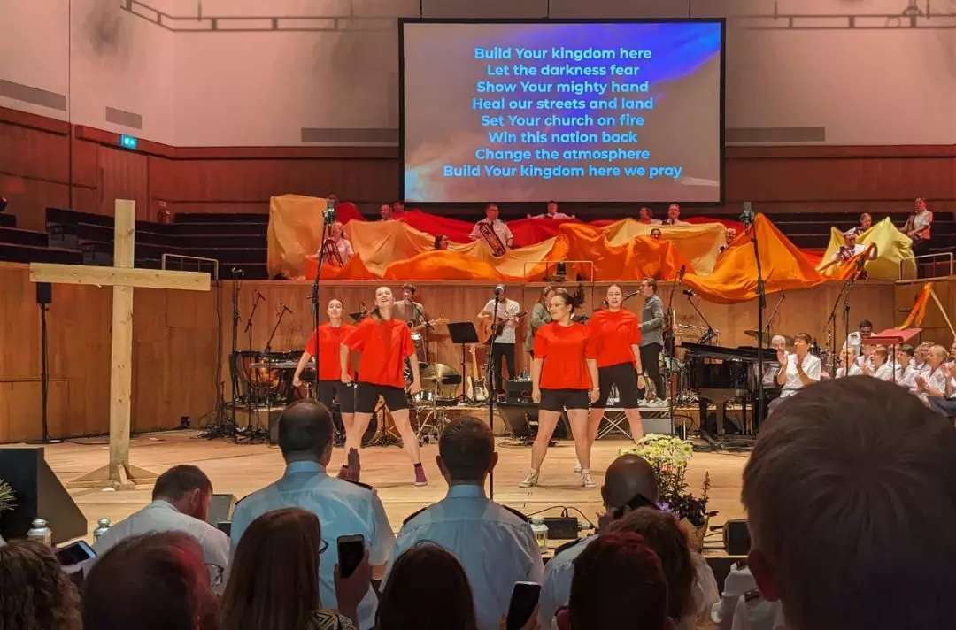 A photo of dancers in red t-shirts and cadets waving orange and yellow fabric