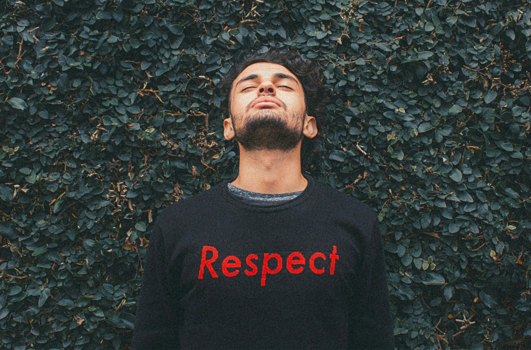 A photo shows a person standing in front of a bush with their eyes closed and wearing a shirt that reads: Respect.