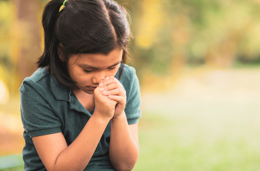 A photo shows a child praying with hands clasped and head bowed.