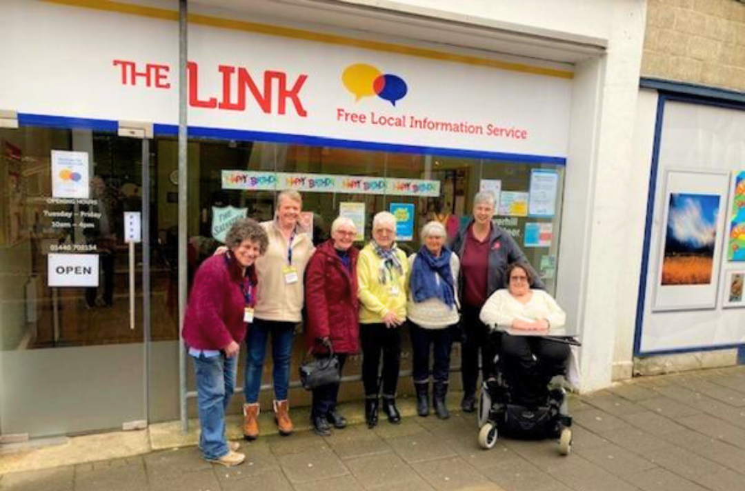 A photo shows the facade of The Link with a smiling team of people standing in front of it.