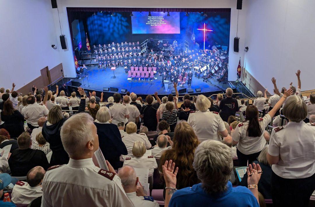 A photo of the congregation worshipping at Together 2024 – many people are standing with their hands in the air