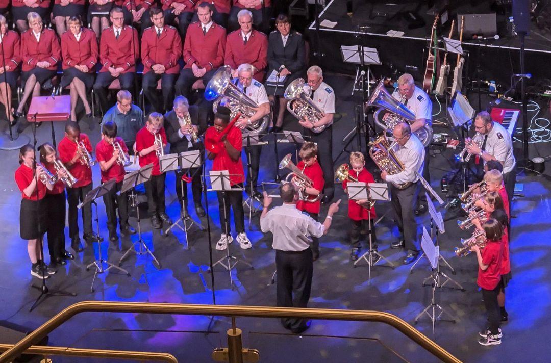 A photo of the Wrexham Community Brass playing on stage at Together 2024, featuring brass players of all ages