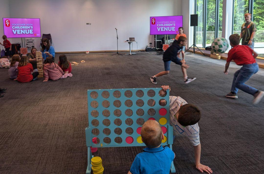A photo of children playing in the Children's Venue at Together 2024. Two boys are playing a giant version of Connect 4, two other boys are playing football and a group of children are playing Jenga