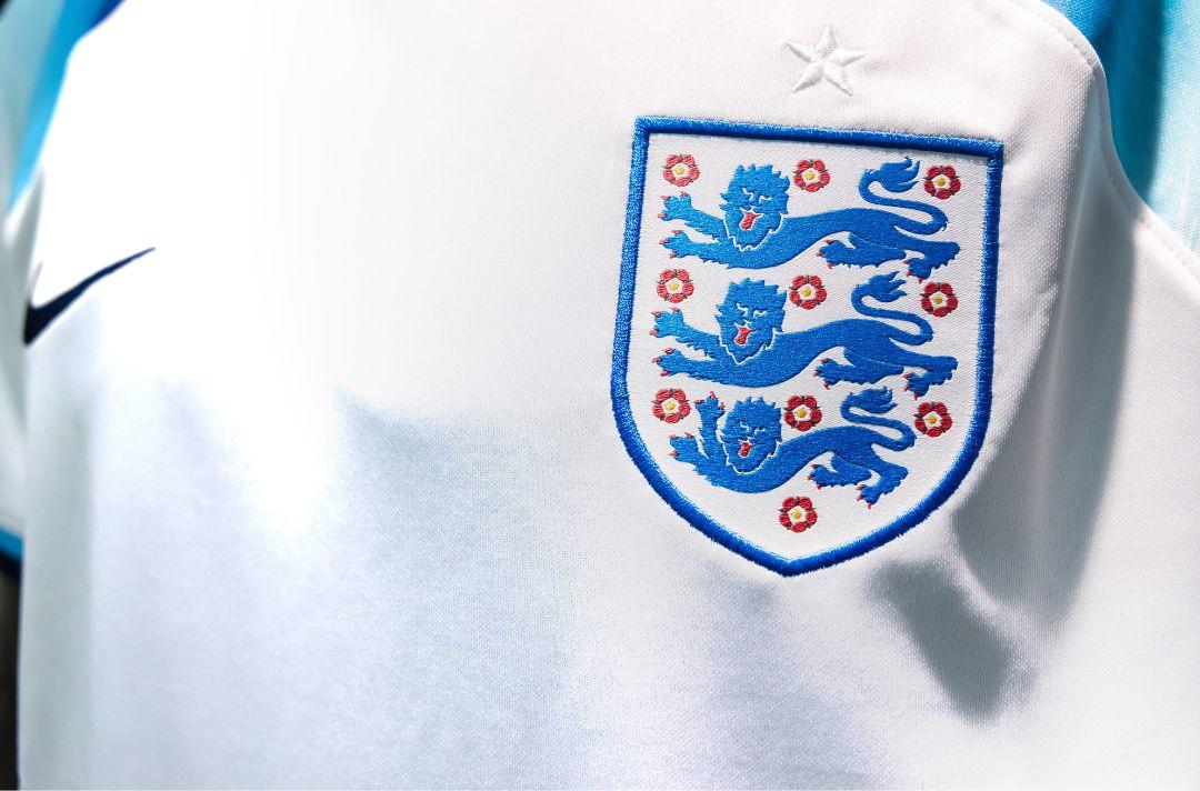 A close-up photo shows the three lions shield on an England football shirt.