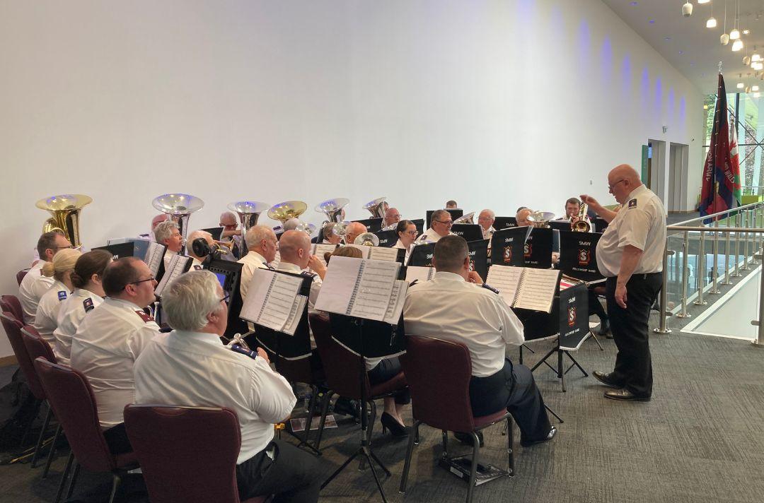 A photo of the South and Mid Wales Fellowship band playing at Together 2024 with a Salvation Army and Welsh flag in the background
