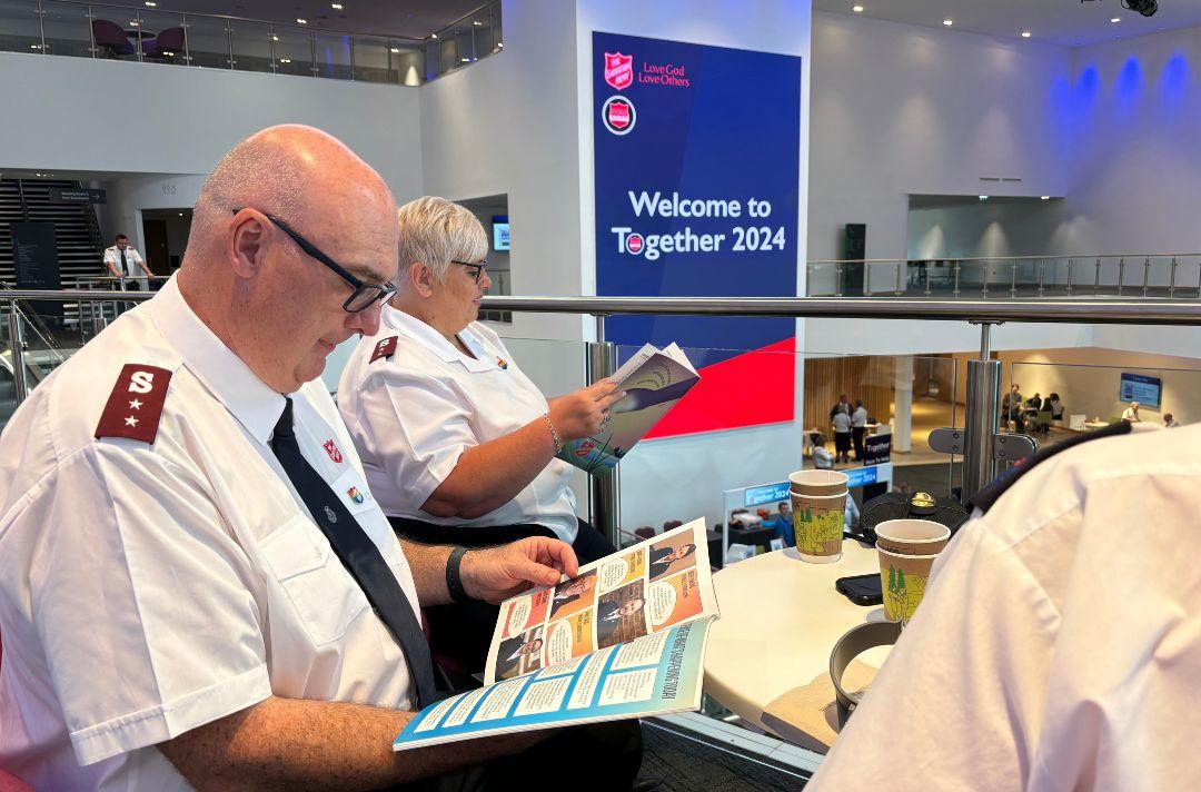 A photo of Salvation Army officers reading the Commissioning brochure in the atrium of ICC Wales